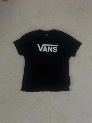 Svart Vans t-shirt med logga - Snygg svart t-shirt från Vans med stor vit logga framtill. Klassisk passform och rund halsringning. Perfekt till jeans eller shorts för en avslappnad streetwear-look.
