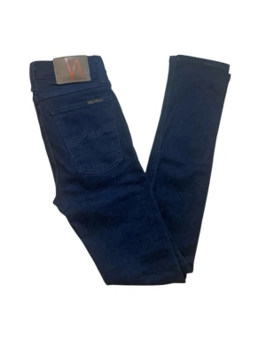 Mörkblå  jeans från Nudie - Snygga mörkblå skinny jeans från Nudie Jeans med klassisk femficksdesign och läderpatch bak i midjan. Jeansen har smal passform och är tillverkade i stretchig denim för extra komfort. Perfekta för dig som gillar en stilren och enkel look.