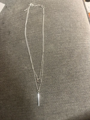 Oanvänt silver halsband (dubbel kedja) – H&M  - Säljer ett helt oanvänt halsband från H&M i silverfärg. Superfint lager-på-lager halsband med ringdetalj + stavberlock. Minimalistiskt och passar till allt!