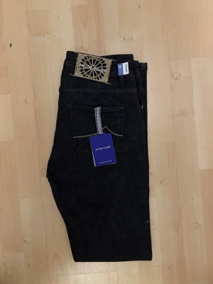 Mörkblå jeans från Jacob Cohen - Snygga mörkblå jeans från Jacob Cohen med klassisk femficksdesign och kontrastsömmar. Jeansen har en unik patch bak i beige och svart samt en blå etikett. Perfekta för dig som gillar stilrena och exklusiva jeans.