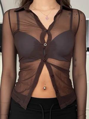 Brun meshskjorta med knappar - Snygg brun meshskjorta med lång ärm och genomskinligt material. Skjortan har flera knappar framtill och en croppad passform som ger en edgy vibe. Perfekt för dig som vill sticka ut och gillar trendiga detaljer. Jag brukar ha S i storlek och den här var väldigt liten på mig.