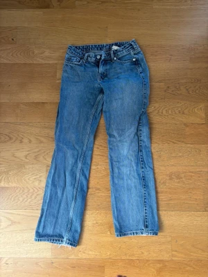 Blå raka jeans med rå kant - Säljer ett par klassiska blå jeans med rak passform och rå, fransad kant nertill. Jeansen har fem fickor och stängs med dragkedja och knapp. Perfekta för en avslappnad och trendig look. Lowwaist