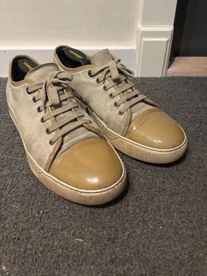 Beige sneakers från Lanvin - Snygga beige sneakers från Lanvin med mockamaterial. Klassisk låg modell med beige snörning och gummisula. Perfekta för dig som gillar stilrena och exklusiva skor med en twist. Pris kan diskuteras vid snabb affär!