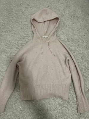 Beige stickad hoodie med huva - Mysig beige stickad hoodie med huva och dragsko. Tröjan har långa ärmar och bred ribbad mudd vid midjan och ärmsluten. Perfekt för en avslappnad och chill stil. Materialet känns mjukt och skönt mot huden.