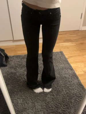 Svarta bootcut jeans med låg midja - Säljer ett par svarta bootcut jeans med låg midja och klassisk femficksdesign. Jeansen har en tight passform upptill och utsvängda ben nertill, vilket ger en snygg siluett. Perfekta för dig som gillar en trendig och avslappnad stil.