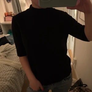 Svart polotopp med halvärm - En svart polotopp med halvärm och rak passform. Toppen har en enkel och stilren design som passar till många olika outfits. Perfekt för dig som gillar en clean och klassisk look.