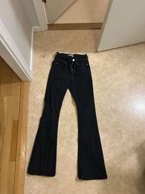 Svarta bootcut jeans med hög midja - Säljer ett par svarta bootcut jeans med mellan midja och klassiska fem fickor. Jeansen har utsvängda ben och stängs med knapp och dragkedja. Perfekta för dig som gillar en retroinspirerad look och vill ha ett par bekväma och snygga jeans. Dom är lite trasiga där nere 