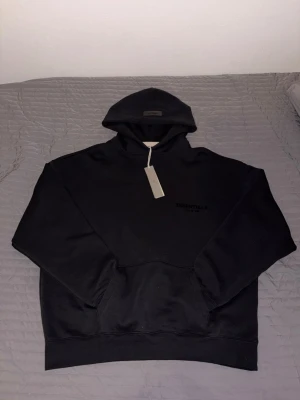 Svart Essentials Fear of God hoodie set  - Säljer en svart hoodie från Essentials Fear of God med tryckt logga på bröstet och ryggen. Den är används några gånger men annars är den i ny skick 