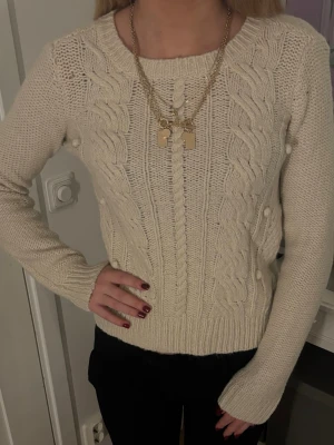 Beige kabelstickad tröja - Snygg beige kabelstickad tröja med rund halsringning och långa ärmar. Tröjan har ett klassiskt flätmönster framtill och ribbstickade muddar vid ärmslut och nederkant. Perfekt för lager-på-lager och passar till det mesta.