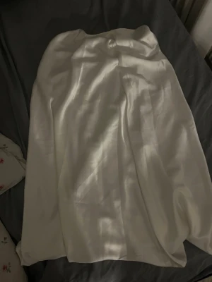 Vit långkjol i silke - Snygg vit långkjol i glansigt silkesmaterial. Kjolen har en enkel och elegant design med mjukt fall och passar perfekt till dig som gillar stilrena plagg. Perfekt att styla med en topp eller stickad tröja. Köpt för 600, säljs för 300