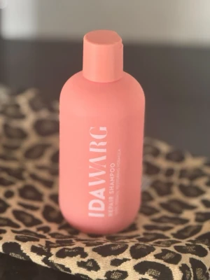 IDAWARG Repair Shampoo rosa flaska - Säljer en rosa flaska IDAWARG Repair Shampoo med vit text på framsidan. Flaskan har rund form och skruvlock. Perfekt för dig som vill ta hand om ditt hår med en vårdande formula.
