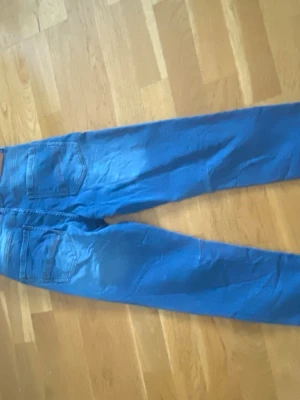Blå raka jeans med fem fickor - Säljer ett par klassiska blå jeans med rak passform och fem fickor. Jeansen har bälteshällor och stängs med dragkedja och knapp. Perfekta för en avslappnad stil och funkar till det mesta. Materialet känns som bomull med lite stretch.