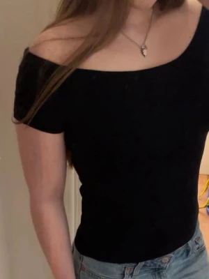 Svart offshoulder topp - Snygg svart offshoulder topp med korta ärmar och figurnära passform. Perfekt att matcha med jeans eller kjol för en trendig look. Enkel och stilren design som passar till många olika outfits.