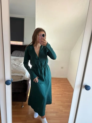 Grön långärmad långklänning - En stilren grön långklänning med v-ringning och långärmar. Klänningen har en markerad midja och är tillverkad i ett mjukt material som ger en skön passform. Perfekt för dig som gillar enkel och klassisk design. Prislapp kvar. Nypris 700kr!