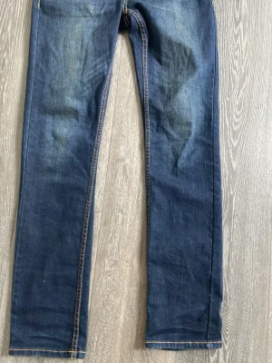 Mörkblå skinny jeans - Säljer ett par mörkblå skinny jeans med klassisk femficksdesign och kontrastsömmar. Jeansen har en smal passform och är tillverkade i ett stretchigt denimtyg som sitter snyggt längs benen. Perfekta till en avslappnad look.
