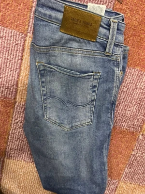 Blå jeans från Jack & Jones - Snygga blå jeans från Jack & Jones med klassisk femficksdesign och ljus tvätt. Jeansen har en skinnpatch med logga bak i midjan och subtila slitningar för en avslappnad look. Perfekta till vardagsstilen och passar till det mesta.