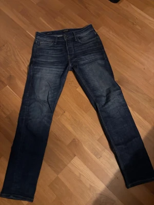 Mörkblå raka jeans - Snygga mörkblå jeans med raka ben och klassisk femficksdesign. Jeansen har diskreta slitningar framtill och är tillverkade i denim. Perfekta för en stilren och avslappnad look. Jeansen är från Jack& Jones som köptes för ca 1 års sen, dom är inte så använda. 