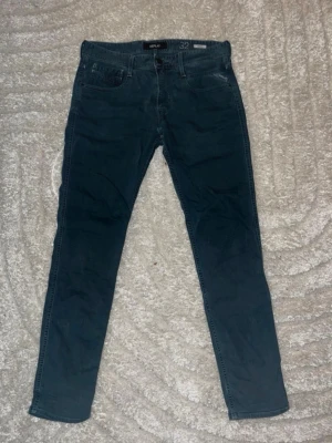 Mörkblå slim fit jeans från Replay - Snygga mörkblå slim fit jeans från Replay med klassisk femficksdesign och diskret broderad detalj på bakfickan. Jeansen har en modern passform och är tillverkade i mjuk denim med lite stretch för extra komfort.