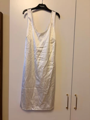 Vit satin klänning med öppen rygg - Stilren vit klänning i satin med en öppen rygg för en snygg design. Är lite osäker på storlek då det inte står men förmodligen en S/M. Helt ny utan prislapp