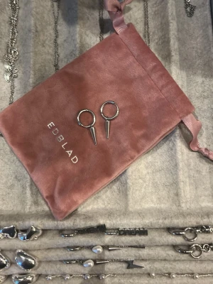 Silvriga örhängen från Edblad - Säljer ett par stilrena silvriga örhängen från Edblad. Örhängena har en rund form med en spetsig hängande detalj, vilket ger en modern och edgy look. Perfekta för dig som gillar minimalistiska smycken med attityd.