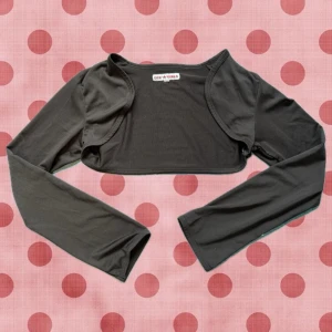 Svart bolerotopp  - Svart bolerotopp med lång ärm och croppad passform. Perfekt att slänga över ett linne eller bandeau för en trendig lager-på-lager-look. Tunn och stretchig i materialet, enkel att styla till olika outfits.