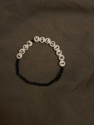 Svart pärlarmband med textpärlor - Armband med svarta små pärlor och vita runda bokstavspärlor som bildar texten 'FUCK VÅLDTÄKT'. Stretchig tråd gör det enkelt att ta på och av. Perfekt för dig som vill göra ett statement med ditt smycke.
