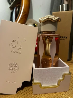 Lattafa TeriAQ parfym 85ml - Lattafa TeriAQ parfym i en elegant glasflaska med guld- och vitdetaljer. Flaskan har en unik form med vita vågiga mönster och ett exklusivt lock med gulddetaljer. Kommer i en stilren beige ask med gulddetaljer. Perfekt för dig som gillar lyxiga och speciella dofter.
