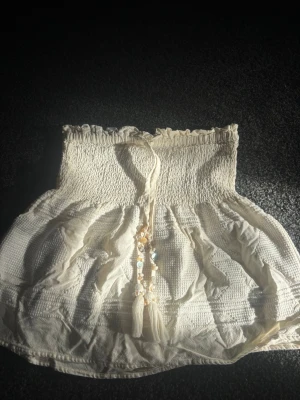 Beige kjol från Zara  - Kjol med smock upptill och dekorativ snörning framtill med pärlor och snäckor. Sälja inte längre. Finns ingen lapp i kjolen med vet att det är storlek xs 