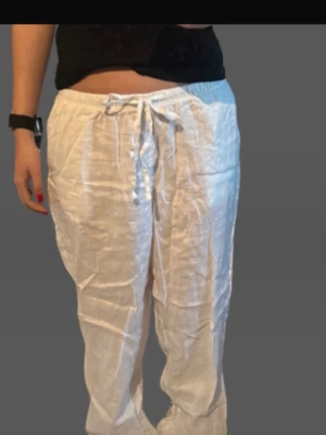 Vita linnebyxor  - Säljer ett par vita linnebyxor med avslappnad passform och elastisk midja med dragsko. Byxorna är tillverkade i svalt linnematerial och har raka ben. Perfekta för en chill och stilren look.