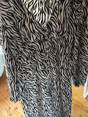 Zebramönstrad långklänning från lager 157 - Säljer en lång zebramönstrad klänning från 157 med v-ringning och knappar framtill. Bra passform med tunt material, perfekt till sommaren💖 köpt nyligen men aldrig använt.