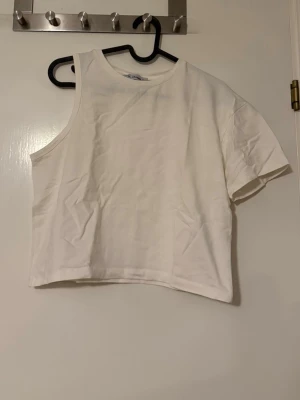 Vit enärmad topp från Chamath - Snygg vit topp från Chamath i bomull. Modellen är croppad och ärmlös på ena sidan, vilket ger en cool asymmetrisk look. Perfekt att styla med jeans eller kjol för en trendig outfit.