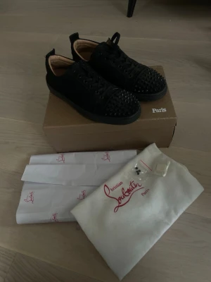 Christian Louboutin skor strl 43 - Hej säljer ett par Snygga svarta sneakers från Christian Louboutin med mattsvarta nitar på tån och sidorna. Skorna är svarta skosnören och är tillverkade i mocka. Kommer med originalkartong, dustbag och extra nitar. Dem är i fint skick och ser riktigt bra ut obs en skadad på ena skon men inget som syns eller märks när du har skon på dig 