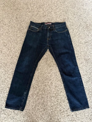 Tommy hilfiger selvedge jeans - Tja, jag säljer ett par mörkblå Tommy Hilfiger selvedge  jeans med rak passform och klassisk femficksdesign. Storlek 31:30! Jeansen har en läderpatch bak i midjan och kontrastsömmar. Tillverkade i slitstark denim, perfekta för en avslappnad och stilren look.