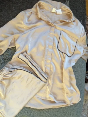 Beige satin pyjamas ser - Så fint pyjamas set, som man ser på sista bilderna har överdelen några få ställen där tråden har släppt lite så att det sticker ut, det finns även några sånna på byxorna och byxorna har en fläck.