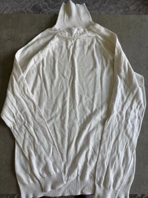 Vit ribbstickad polotröja - Snygg vit polotröja i ribbstickat material med lång ärm och hög krage. Tröjan har en klassisk och clean look, perfekt att styla med jeans eller kjol. Materialet känns mjukt och följsamt mot huden.