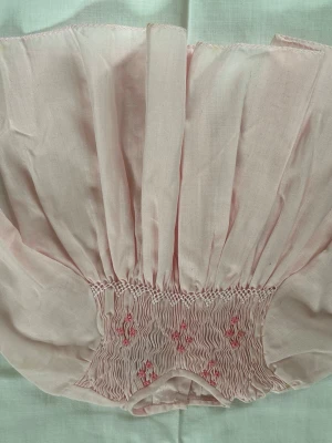 Rosa vintage blus med brodyr - Söt ljusrosa babyklänning i tunn bomull med handsydd smock och små broderade blommor framtill,  puffärmar med resår och knappar i ryggen. Perfekt till babyns första midsommar.