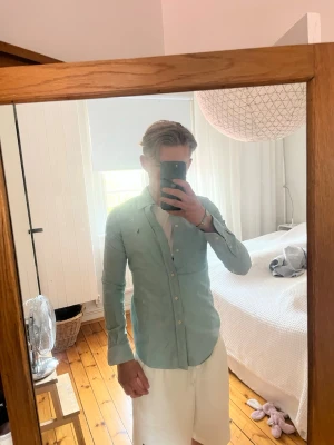 Ljusblå skjorta från Ralph Lauren - Snygg ljusblå skjorta från Ralph Lauren med klassisk krage och knappar framtill. Skjortan har lång ärm och den ikoniska broderade loggan på bröstet. Perfekt till jeans eller chinos för en clean och stilren look.Storlek S 