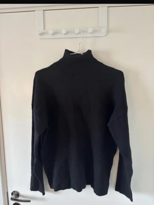 Svart polotröja från Zara - Snygg svart stickad polotröja från Zara med lång ärm och hög krage. Tröjan är enkel och stilren, perfekt att matcha med jeans eller kjol. Materialet är mjukt och bekvämt, och den ribbade kragen ger en extra touch.