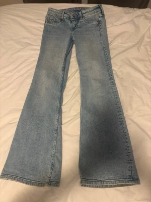Ljusblå bootcut jeans - Säljer ett par ljusblå bootcut jeans med klassisk femficksdesign och normal midja. Jeansen har utsvängda ben och är tillverkade i denim med lätt tvättad look. Perfekta för dig som gillar retrostil och vill ha ett par snygga jeans med avslappnad passform.