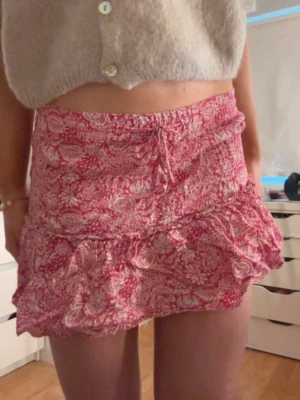 Rosa blommig volangkjol med snörning - Supersöt kort kjol i rosa med vitt blommönster och volangkant. Kjolen har snörning i midjan och inbyggda shorts. Den är perfekt för varma dagar. Lätt och luftig modell som ger en avslappnad och trendig vibe. 💗💗