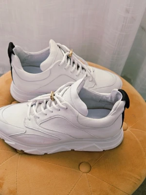 Chunky vita sneakers med svart detalj st 38 - Stilrena chunky sneakers i vitt med svart detalj på hälen. Skorna har en tjock sula och är tillverkade i slätt syntetmaterial med vita snören. Perfekta för dig som gillar en clean och modern look.