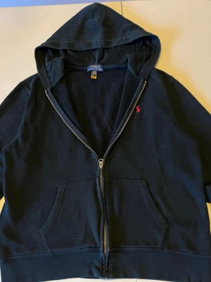Ralph Lauren zip hoodie - Jag säljer en riktigt snygg svart Ralp Lauren zip hoodie med ett litet rött polo märke på bröstet. Storleken är 170/88. Har inte använts så mycket så den har fint skick, inga fläckar eller hål. Priset än inte helt ristat i sten.