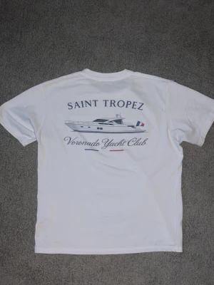 Voronado Yacht Club t-shirt - Vit t-shirt från Voronado Yacht Club med tryck av en yacht och texten 'Saint Tropez' på ryggen. Framsidan har en liten logga på bröstet. Klassisk passform och rund halsringning, perfekt för en avslappnad stil.