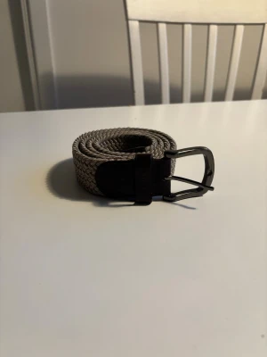 Beige flätat bälte från BOSS - Stilrent beige flätat bälte från BOSS med mörkbruna skinn-detaljer och metallspänne. Perfekt accessoar för att lyfta din outfit med en klassisk touch. nypris runt 800kr. 105 cm