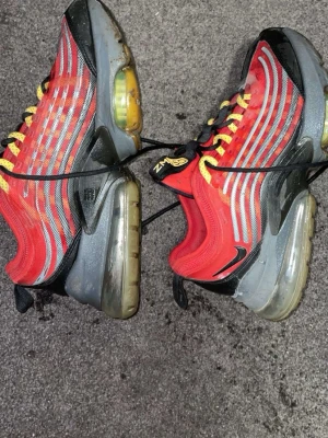 Nike Air Max 720 röda sneakers - Nike Air Max 720 sneakers i rött med svarta och grå detaljer samt reflekterande silverränder. Skorna har gula snören och en stor synlig Air Max-sula som ger en futuristisk vibe. Swoosh-logga på sidan och meshmaterial för extra andningsförmåga.