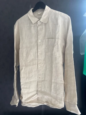 Beige linneskjorta från Arket - Stilren beige skjorta i linne med klassisk krage, perfekt för en avslappnad men snygg look.