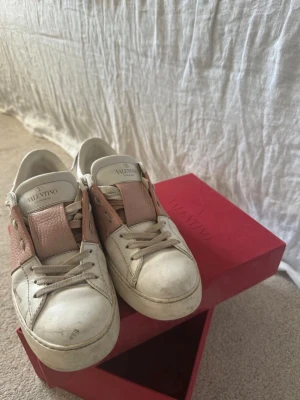 Valentino Garavani vita sneakers - Snygga vita sneakers från Valentino Garavani med detaljer i ljusrosa läder och klassisk logga på plösen. Skorna har låga skaft, vita snören och en chunky sula. Perfekta för dig som gillar exklusiv och trendig streetstyle.