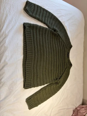 Olivgrön stickad tröja från Bik Bok - Säljer en olivgrön stickad tröja från Bik Bok. Tröjan har ett grovt ribbstickat mönster, rund halsringning och långa ärmar. Perfekt för kalla dagar och enkel att matcha med jeans eller kjol.