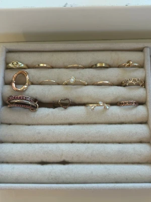 Mix av guldringar med stenar och former - Säljer ett set med flera guldfärgade ringar i olika former och designer. Några ringar har gnistrande stenar, hjärtform, organiska former och detaljer som små pärlor. Perfekt för dig som gillar att mixa och matcha olika stilar.