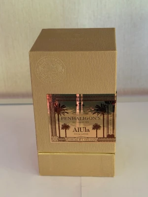 Penhaligon's AlUla Eau de Parfum - Lyxig parfym Penhaligon's AlUla i en elegant guldig kartong med kopparfärgad etikett och palmmotiv. Eau de Parfum, 100 ml. Förpackningen har exklusiv känsla och är tillverkad av kartong med metallisk detalj.